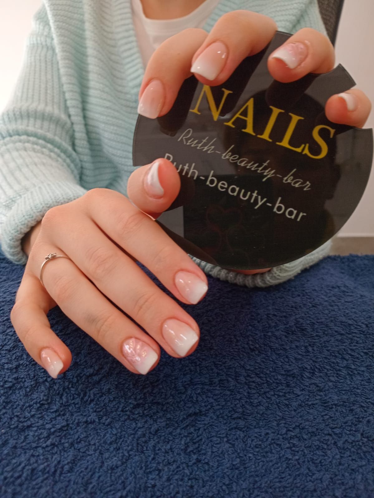 Hands with a light pink and white ombre manicure, holding a circular black sign for
