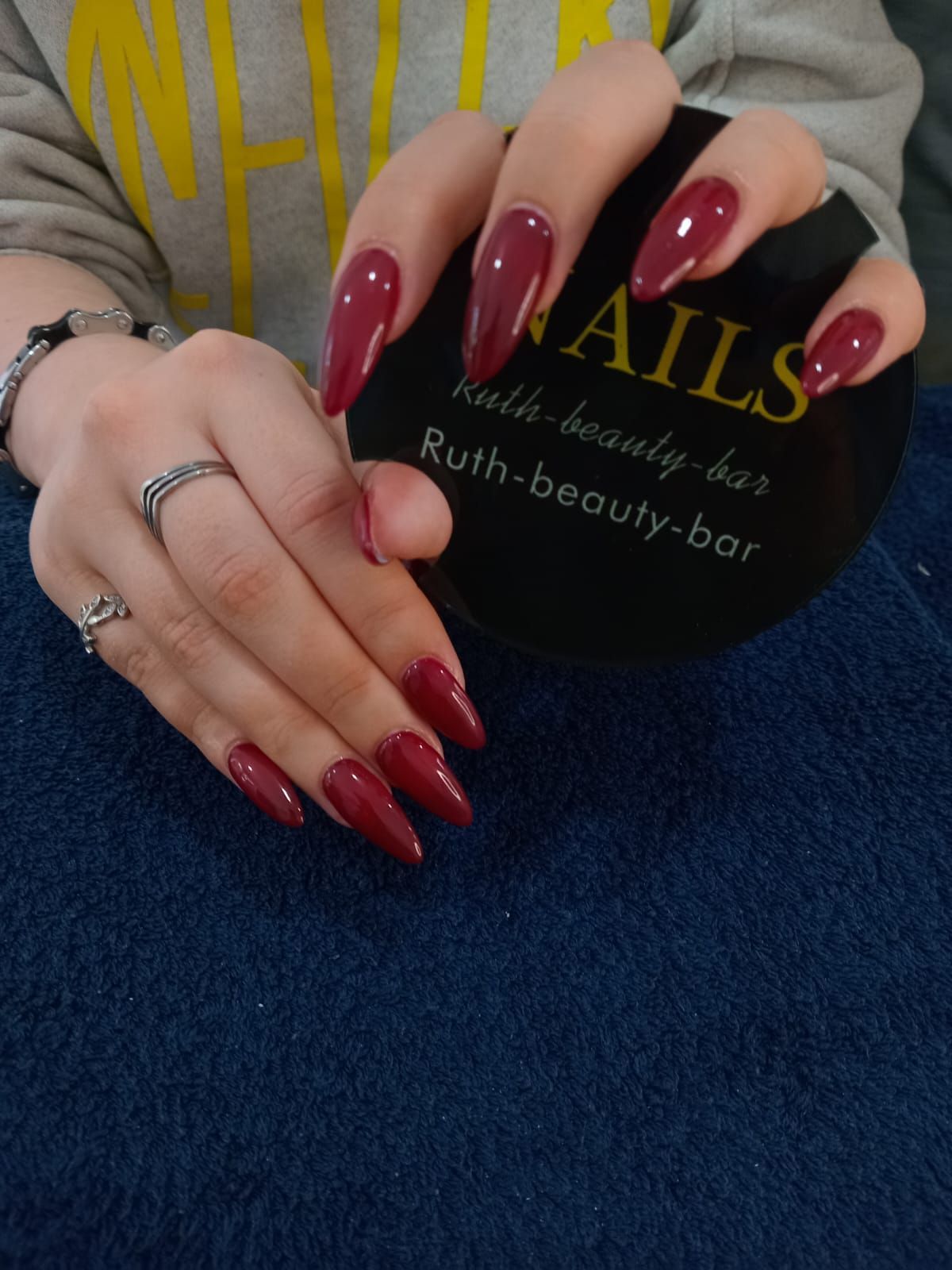 Hands with long, deep red almond-shaped nails holding a black circular sign that reads