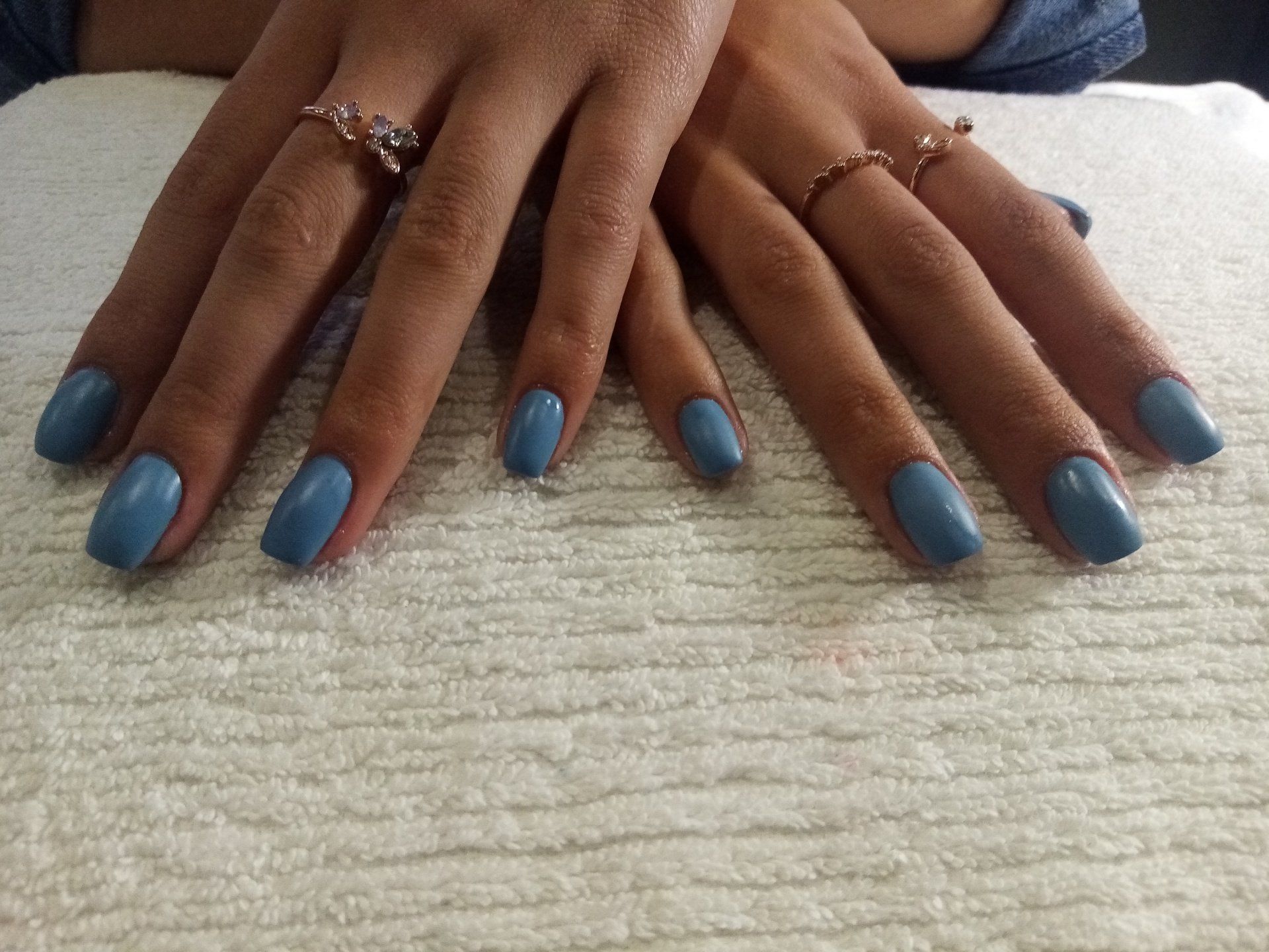 A woman 's hands with blue nails and rings on them