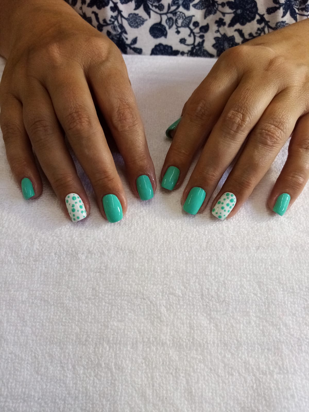 A woman 's hands with green and white nails on a white towel.