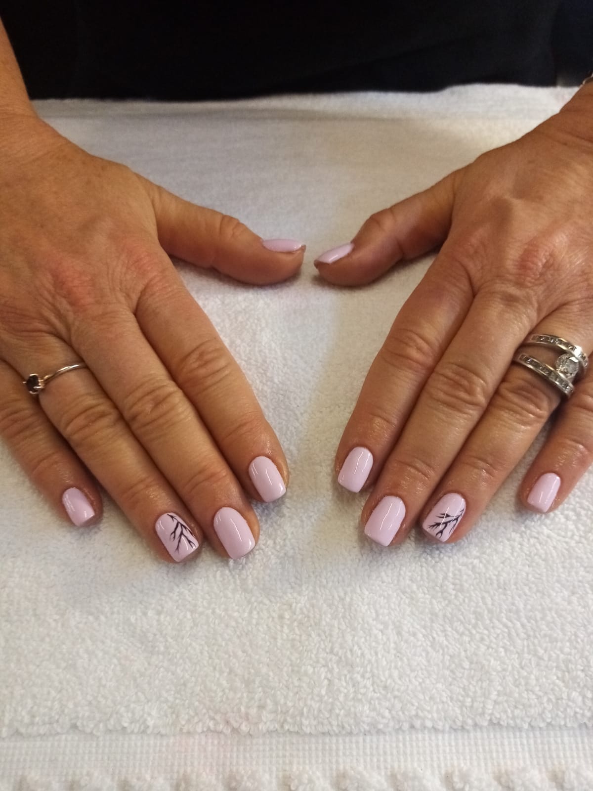 A woman 's hands with pink nails and rings on a white towel.
