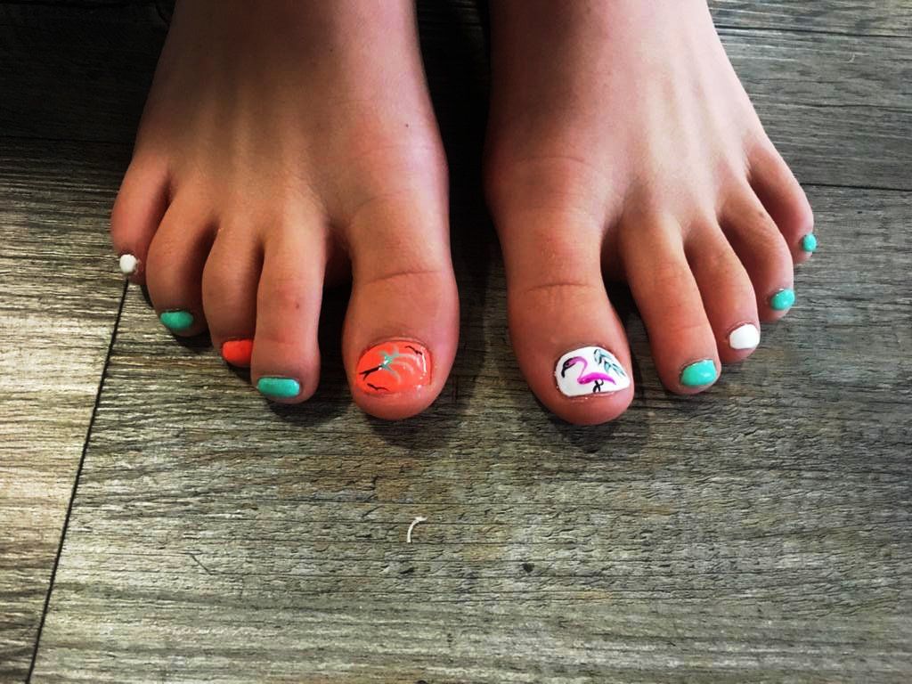 A close up of a person 's feet with colorful nails on a wooden floor.