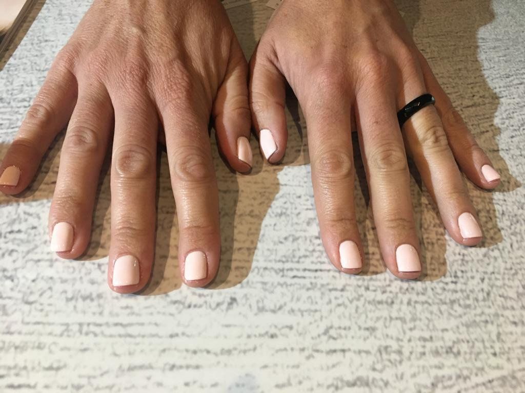 A close up of a woman 's hands with pink nails and a black ring.