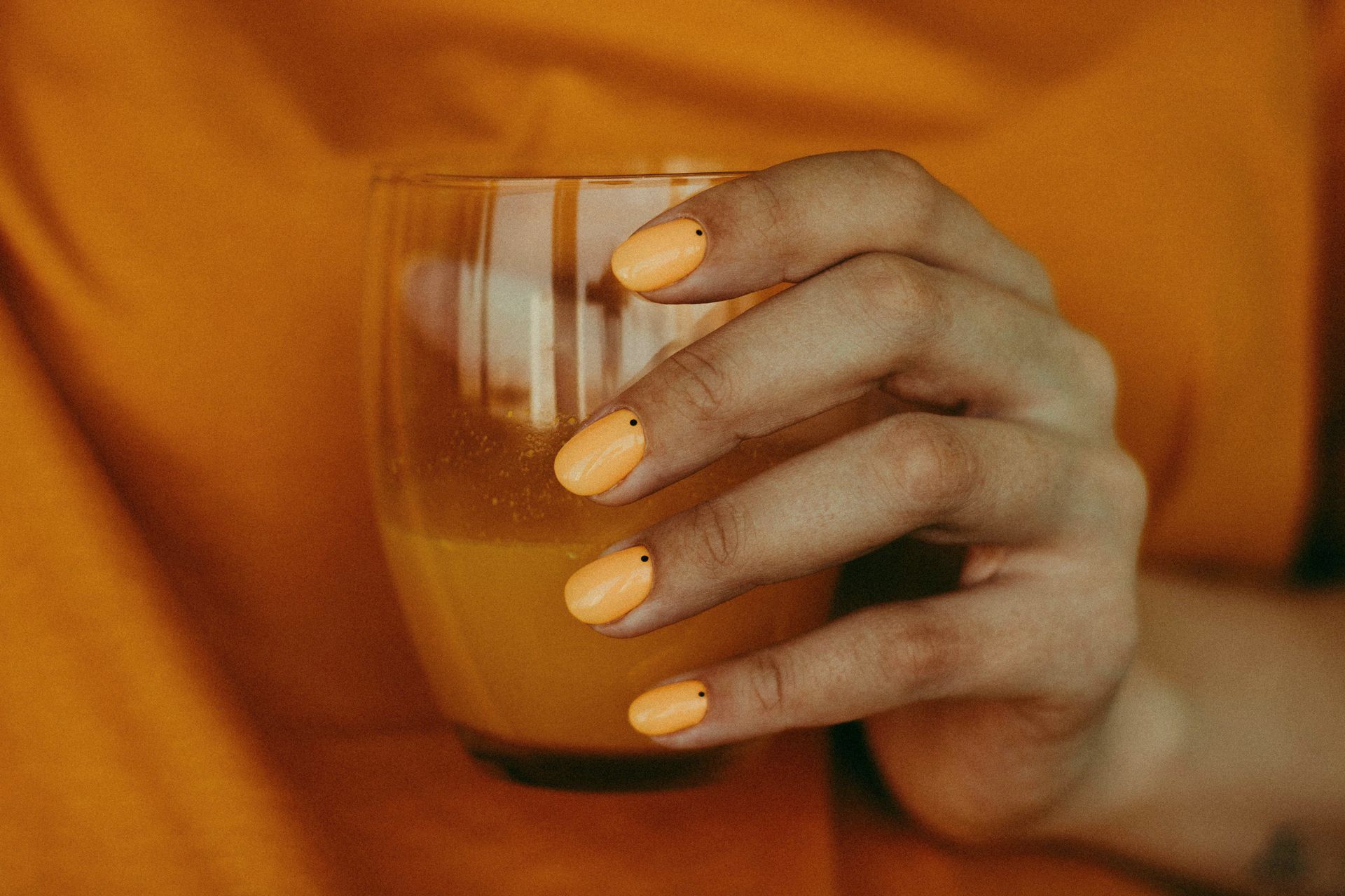 A woman with yellow nails is holding a glass of orange juice.