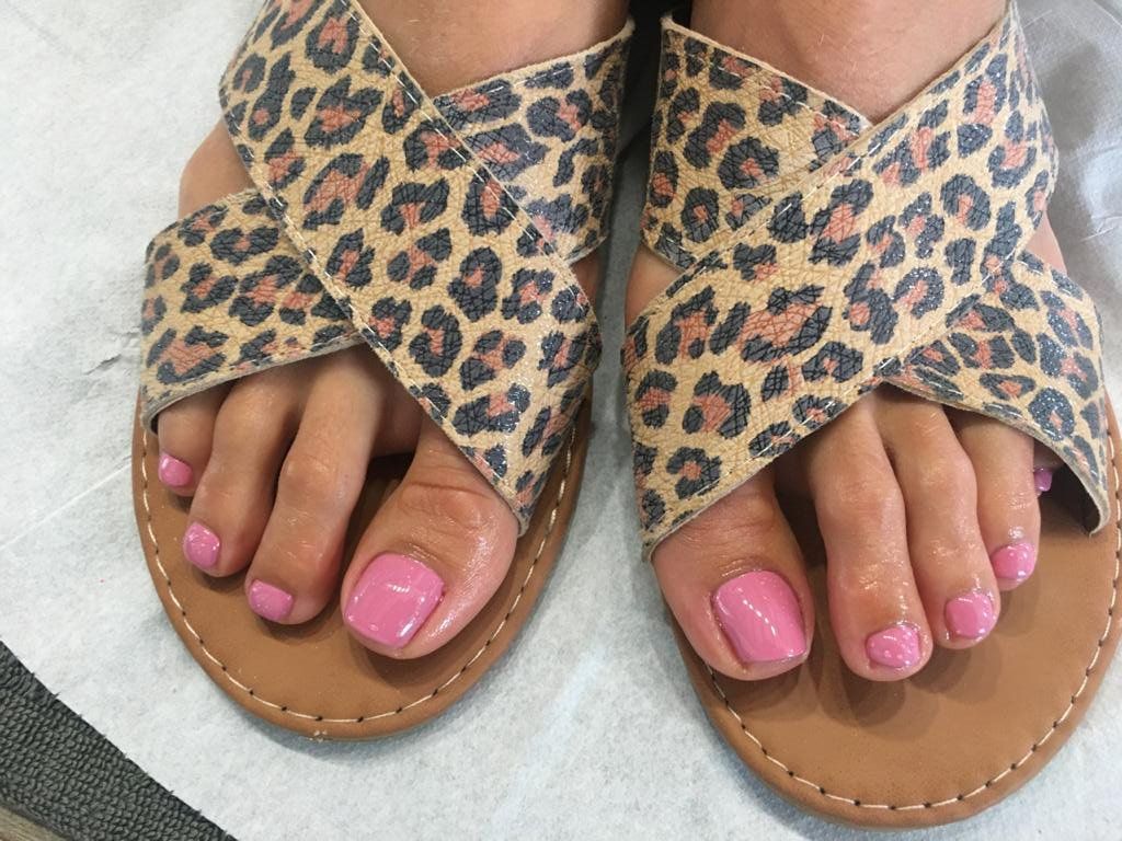 A woman wearing a pair of leopard print sandals with pink toenails.
