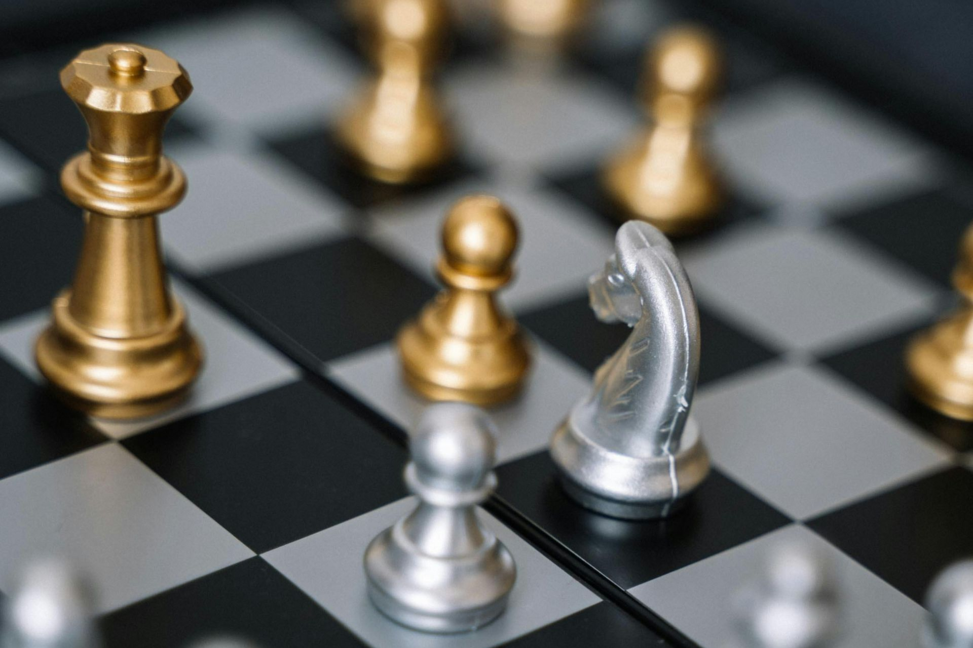 Gold and silver chess pieces on a board, with a silver knight and a gold queen as focal points.