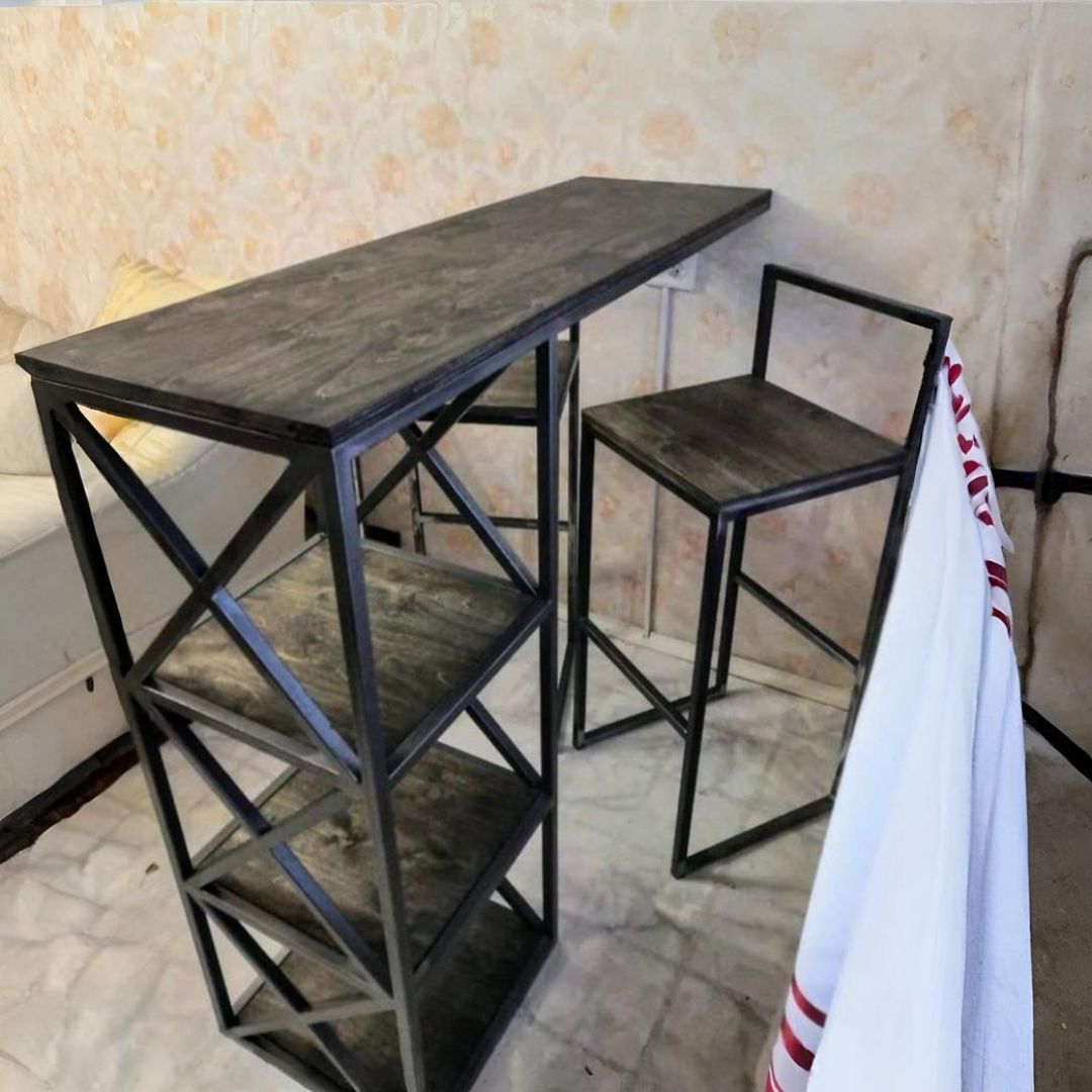 Mesa de bar de metal y madera con estantes adjuntos, taburete y tela blanca en esquina.
