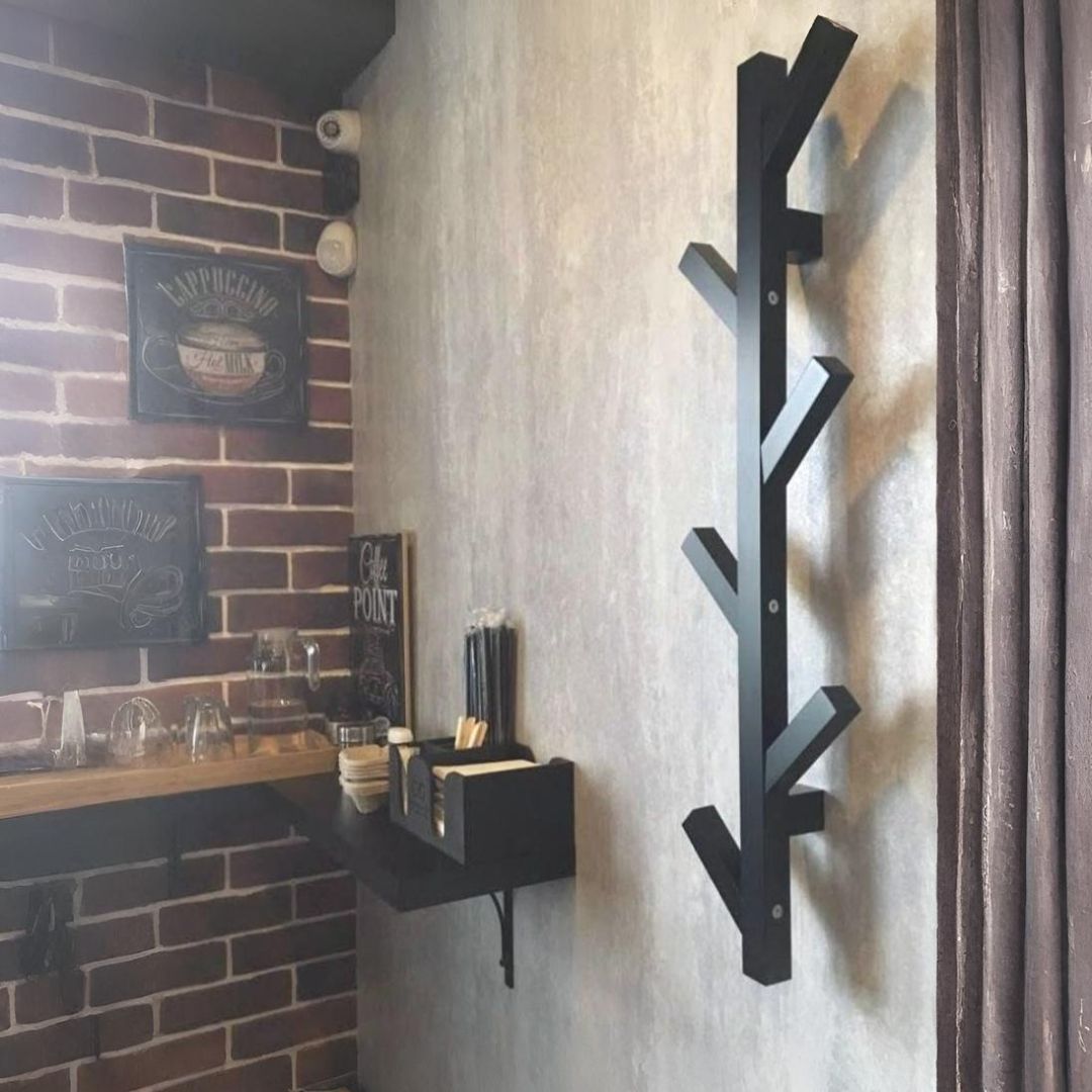 Un perchero negro con forma de árbol sobre una pared gris al lado de una pared de ladrillos y una cortina marrón.