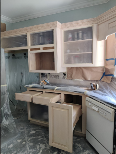 Kitchen cabinets being refinished; some doors and drawers open, covered in plastic.