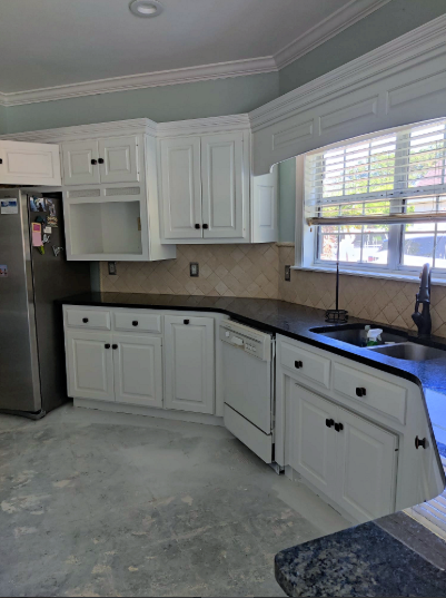 White kitchen cabinets with black countertops, stainless steel appliances, and a window.