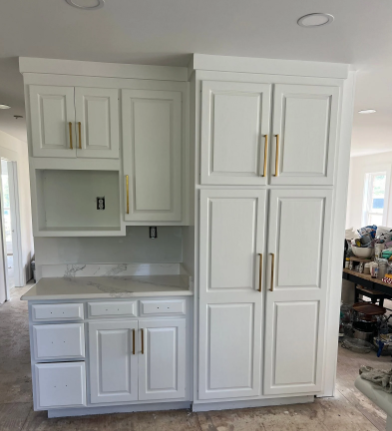 White kitchen cabinets with gold hardware, a built-in pantry, and counter space, under construction.