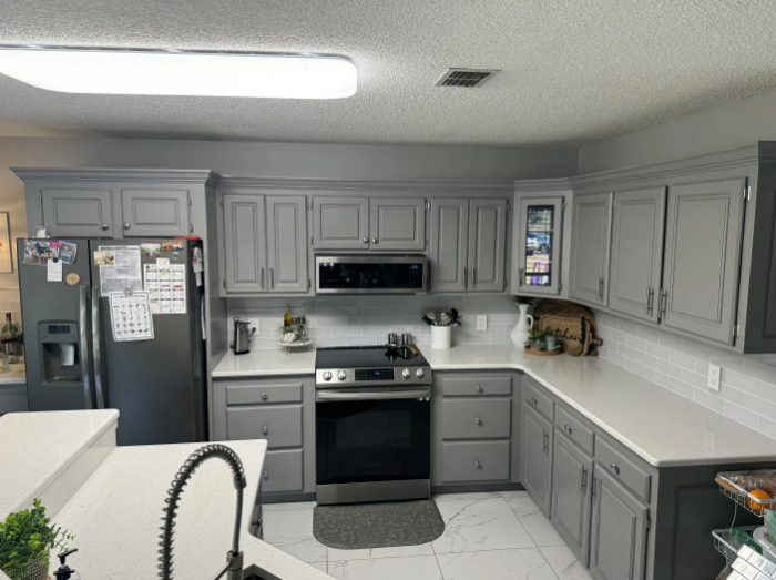 Grey kitchen cabinets and appliances with white countertops.