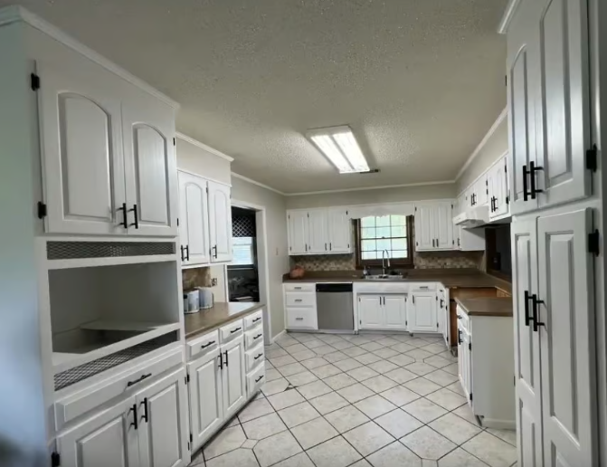 White kitchen with cabinets, tiled floor, and stainless steel appliances.