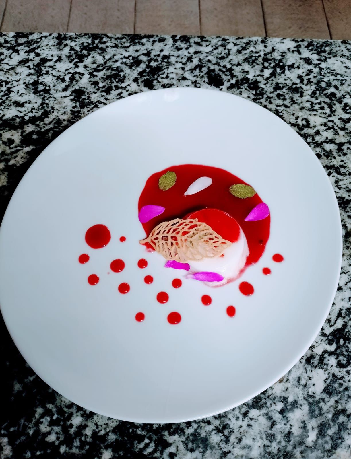 Un piatto con un dessert caratterizzato da salsa rossa, pois e una pallina con una guarnizione a reticolo.