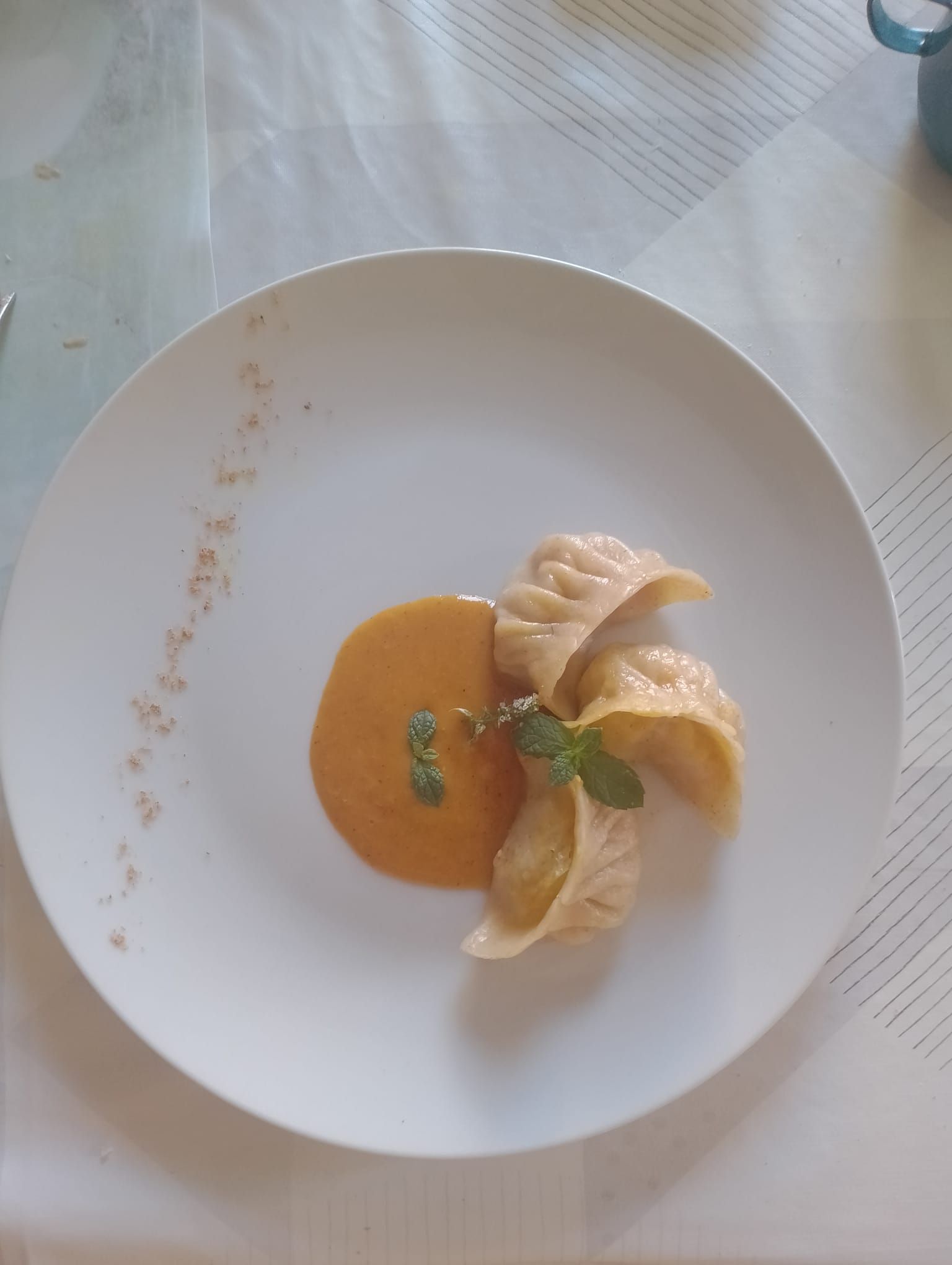 Piatto bianco con gnocchi e salsa all'arancia, guarnito con menta.