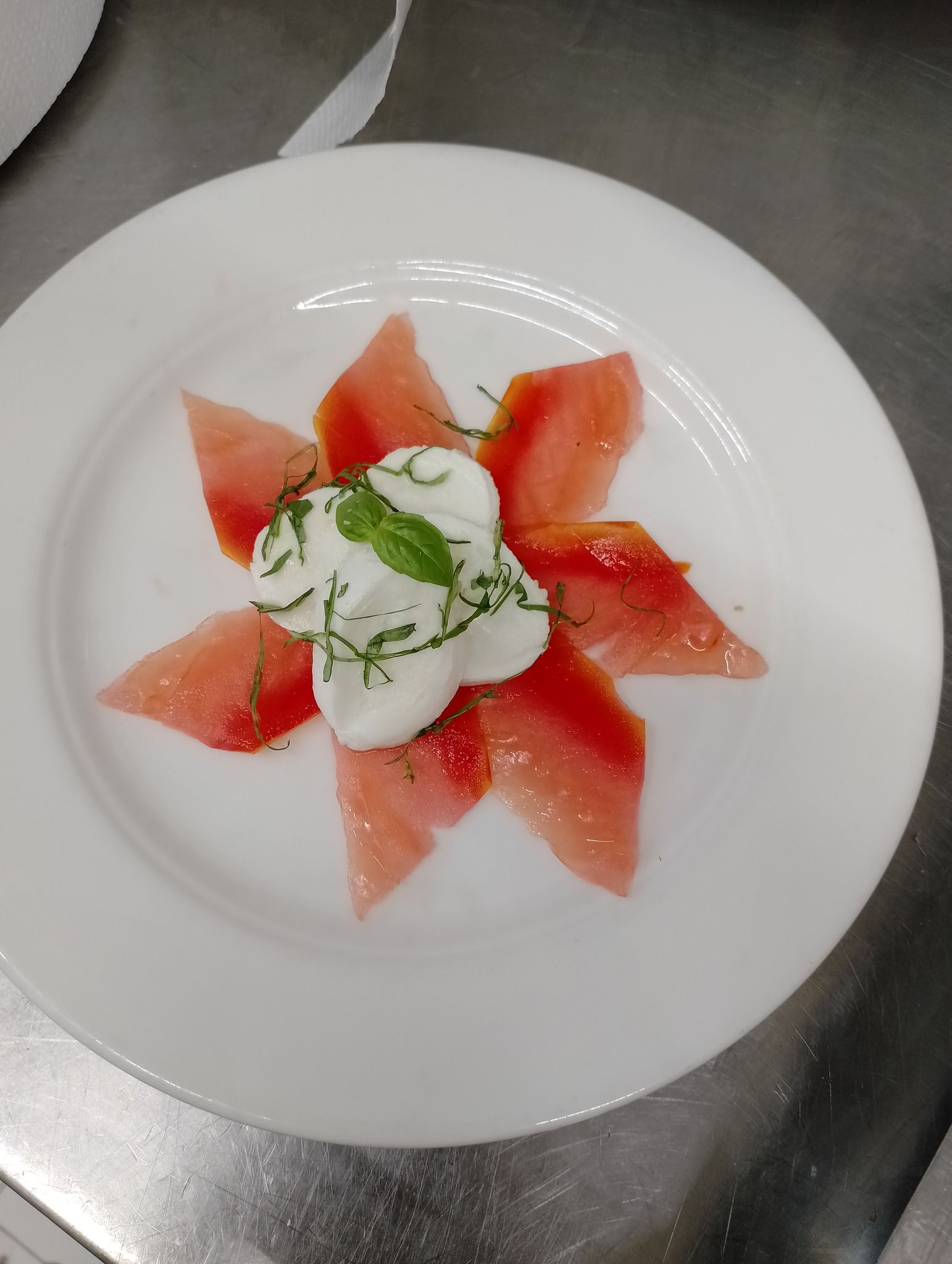 Piatto con fette di anguria disposte a stella, guarnite con formaggio bianco e basilico.