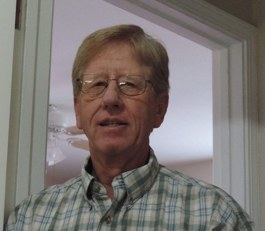 A man wearing glasses and a plaid shirt is standing in a doorway
