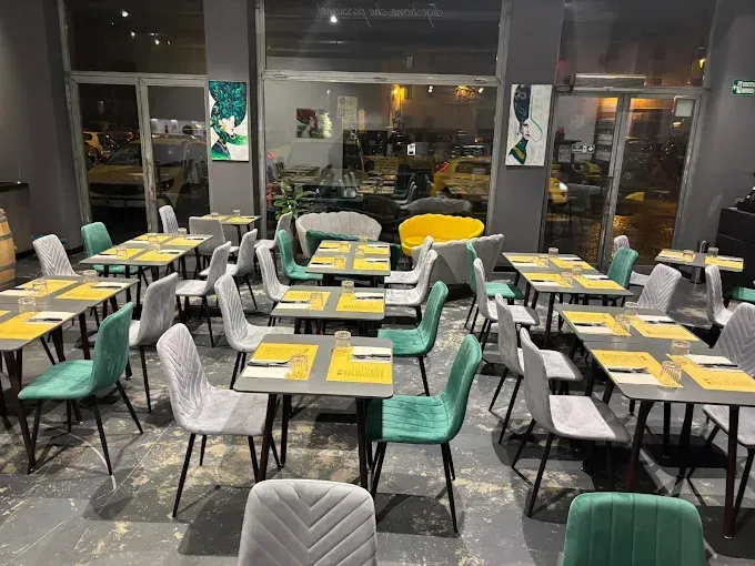 La sala da pranzo di un ristorante moderno, con tavoli grigi, sedie grigie e diverse poltrone in velluto verde disposte in file.