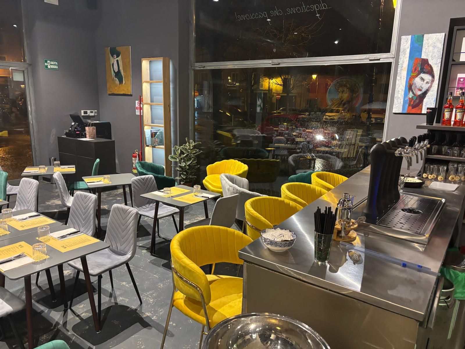 Un interno luminoso e moderno di un ristorante, caratterizzato da diversi tavoli con sedie grigie e sedie curve di un giallo acceso.