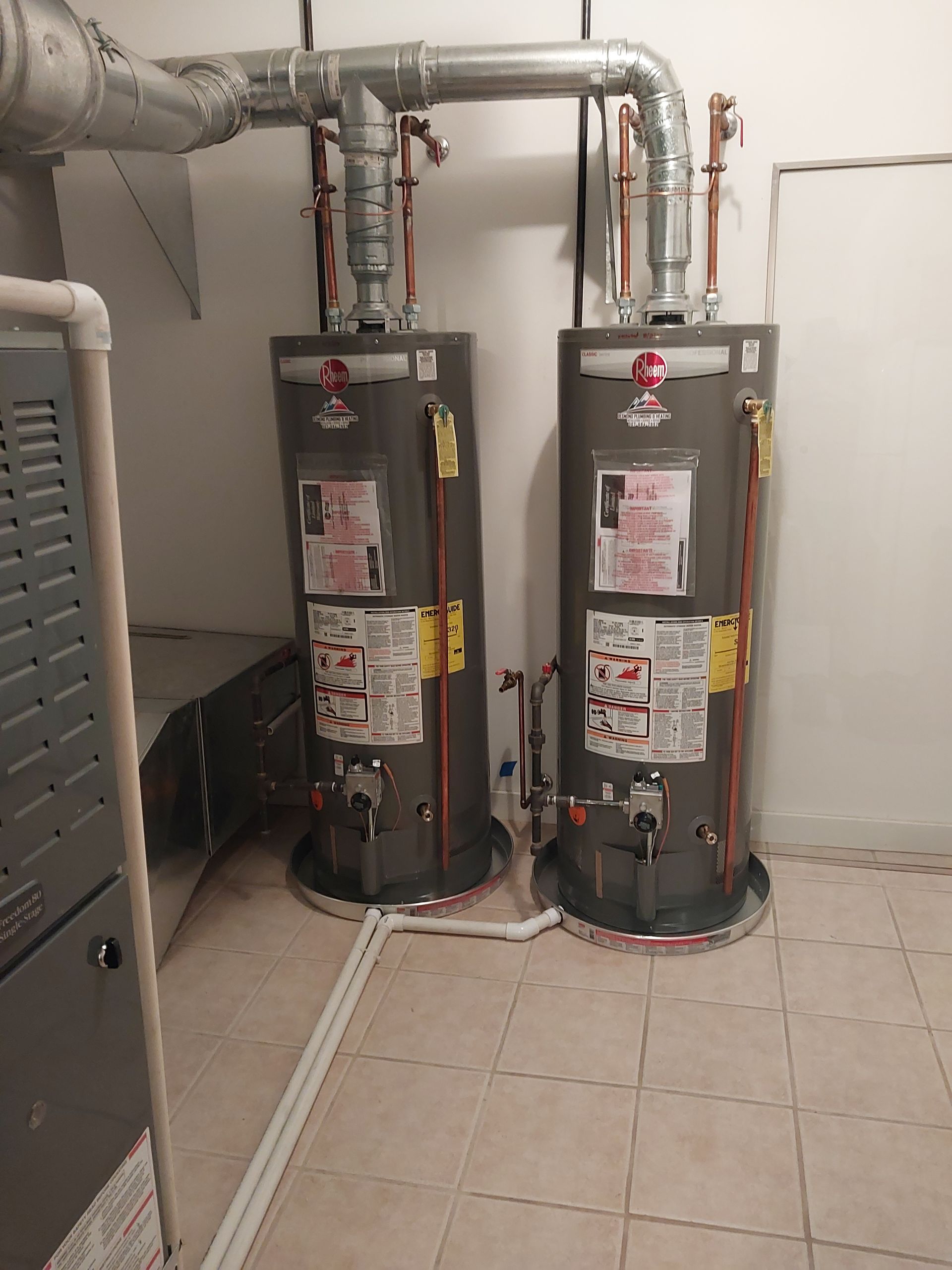 Two tall, gray water heaters with copper pipes in a utility room.