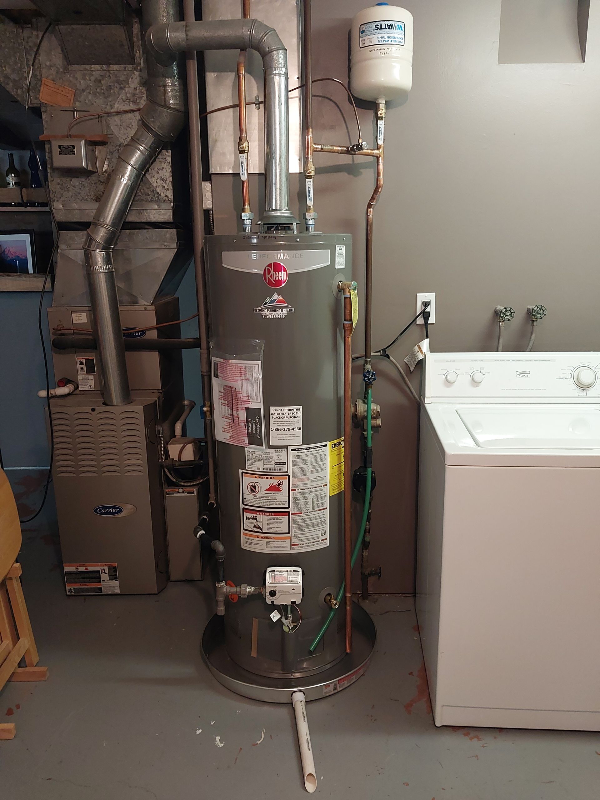 A water heater, furnace, and washing machine are in a basement. The water heater is gray.