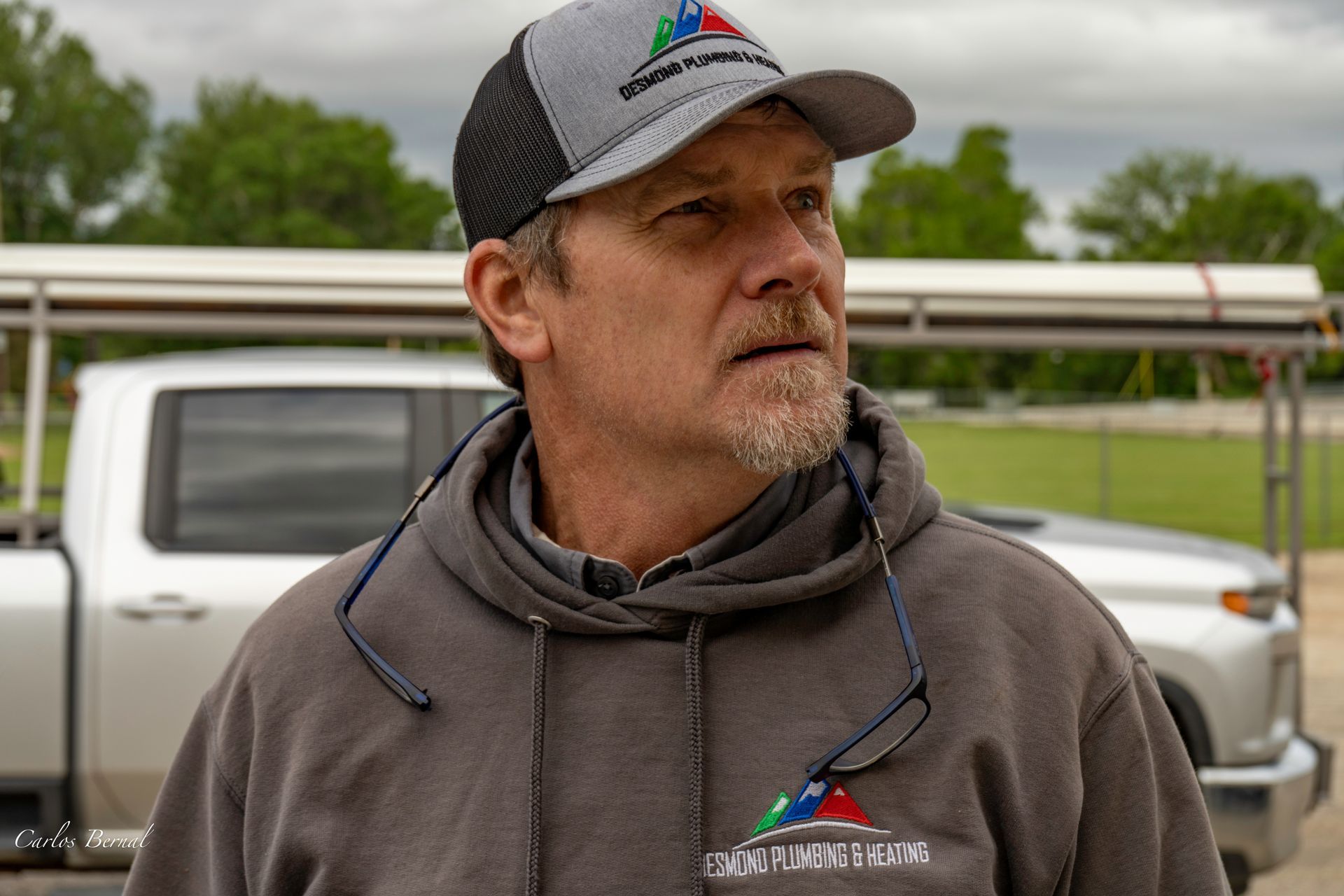 Man wearing a gray hat and hoodie with a logo, looking off to the side, outdoors near a truck.