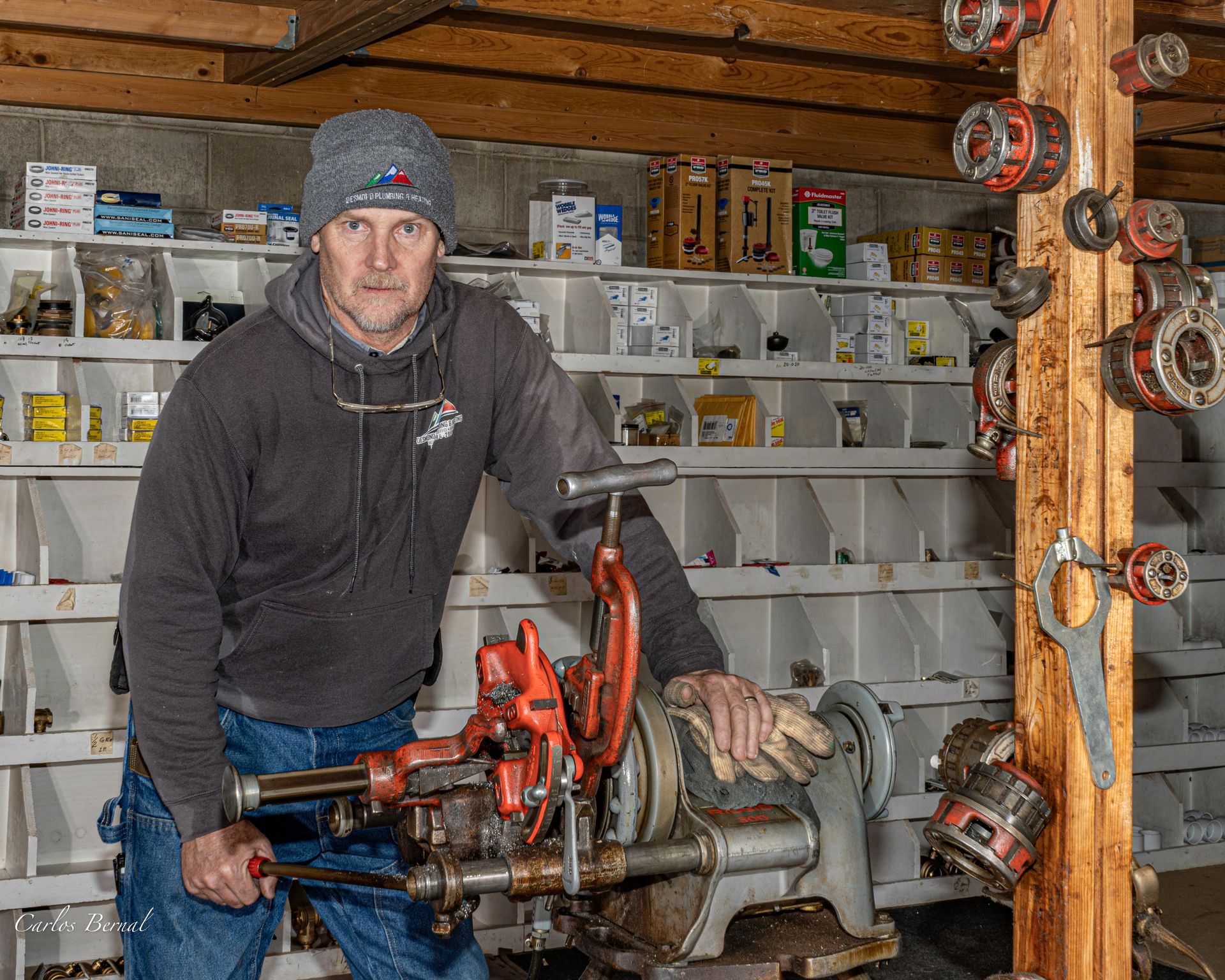 Man using a pipe threading machine, in a workshop setting with shelves of parts.