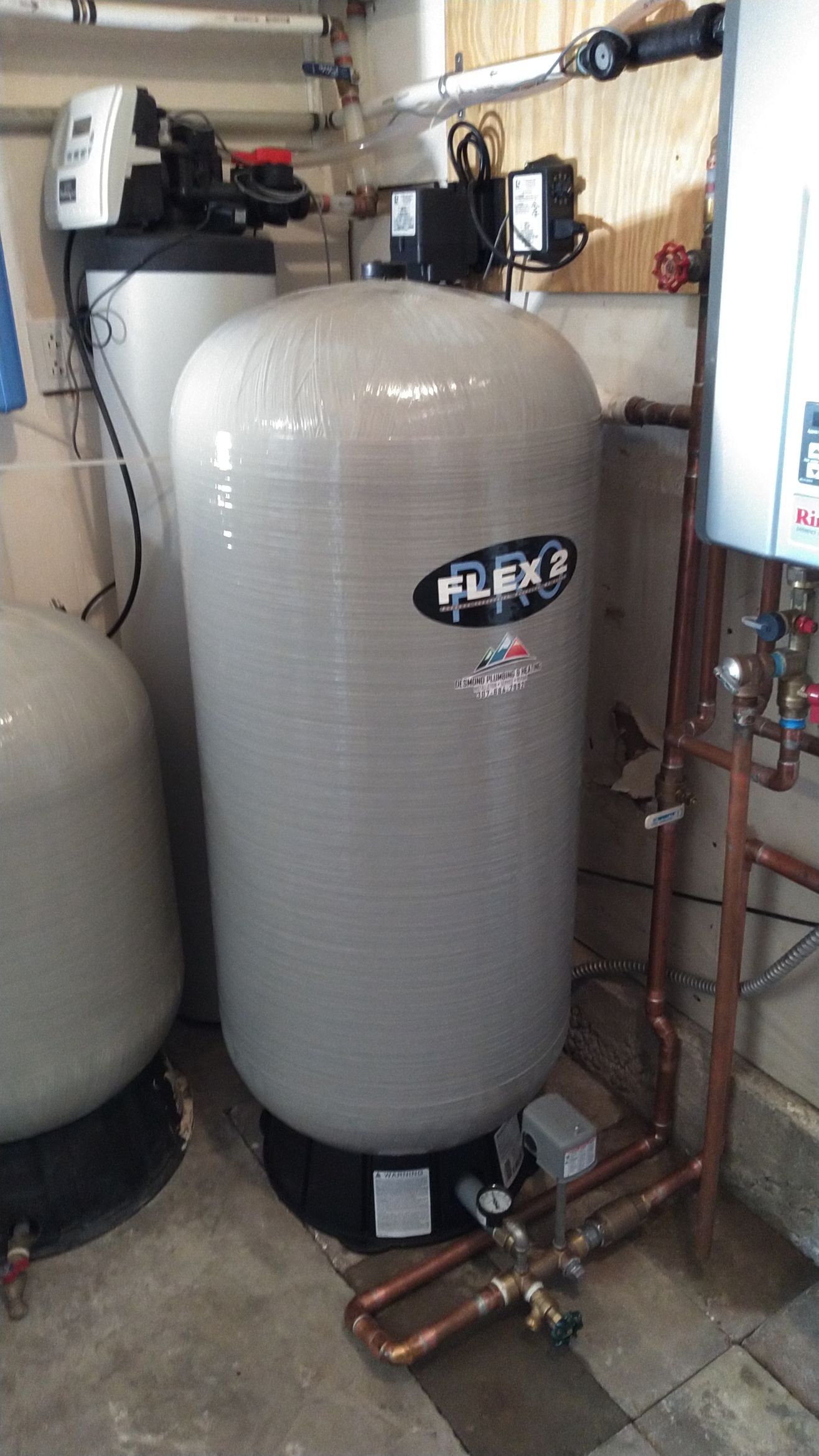 Water softener system in a basement setting with three tanks and copper piping.