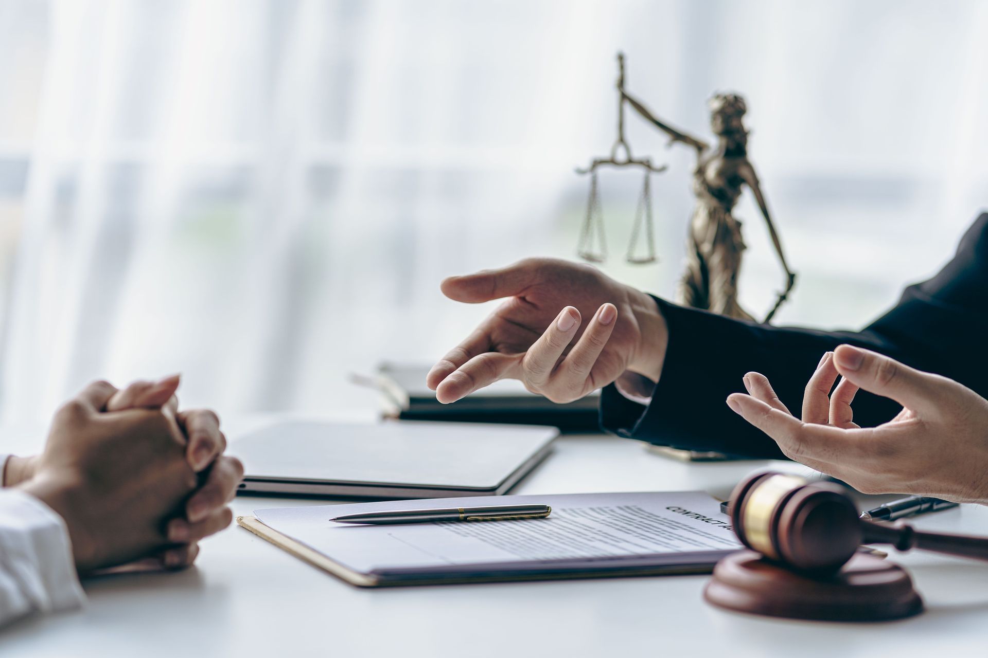 a lawyer is talking to a client while sitting at a table with a statue of justice in the background