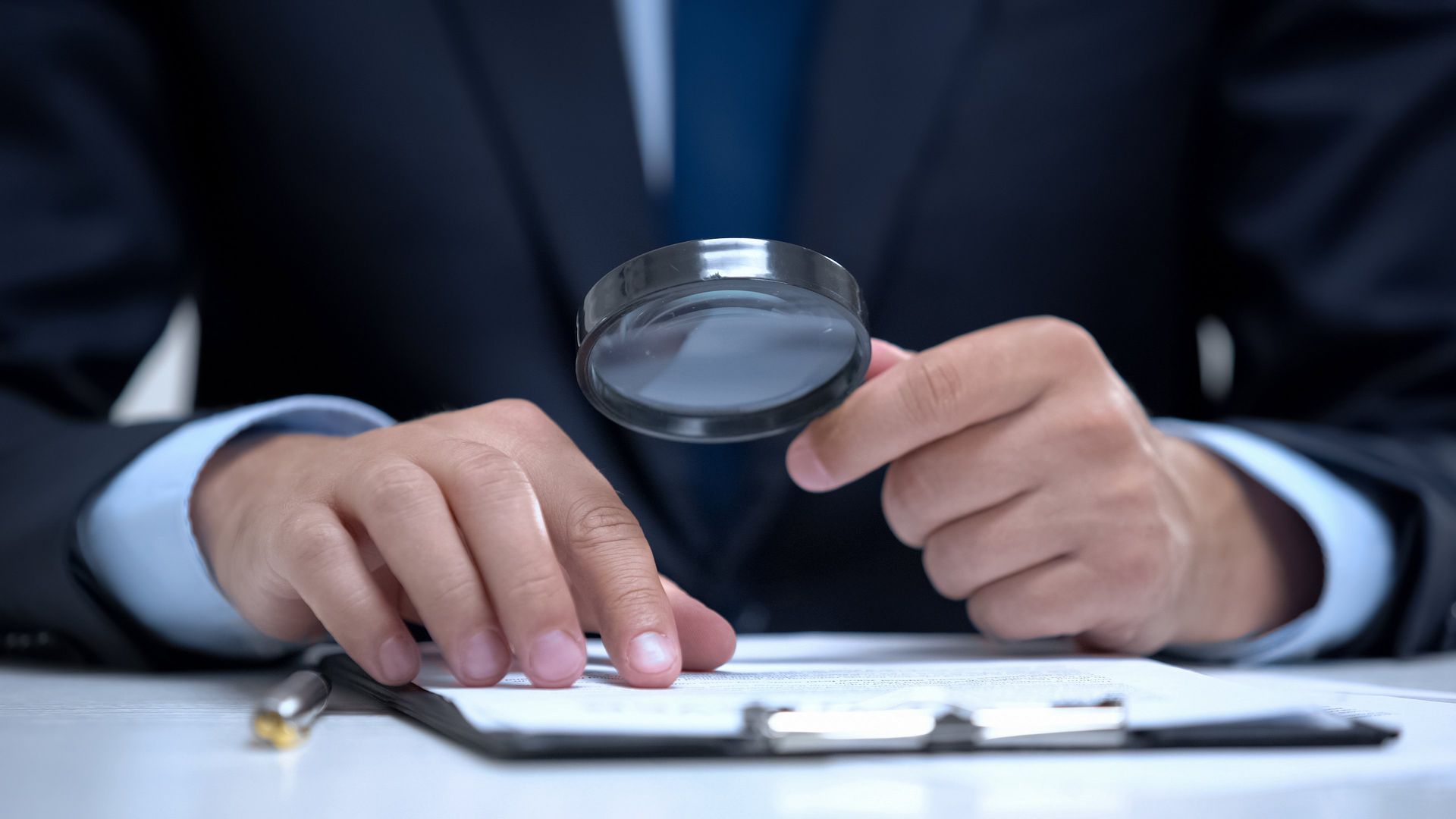 a man in a suit is holding a magnifying glass over a clipboard
