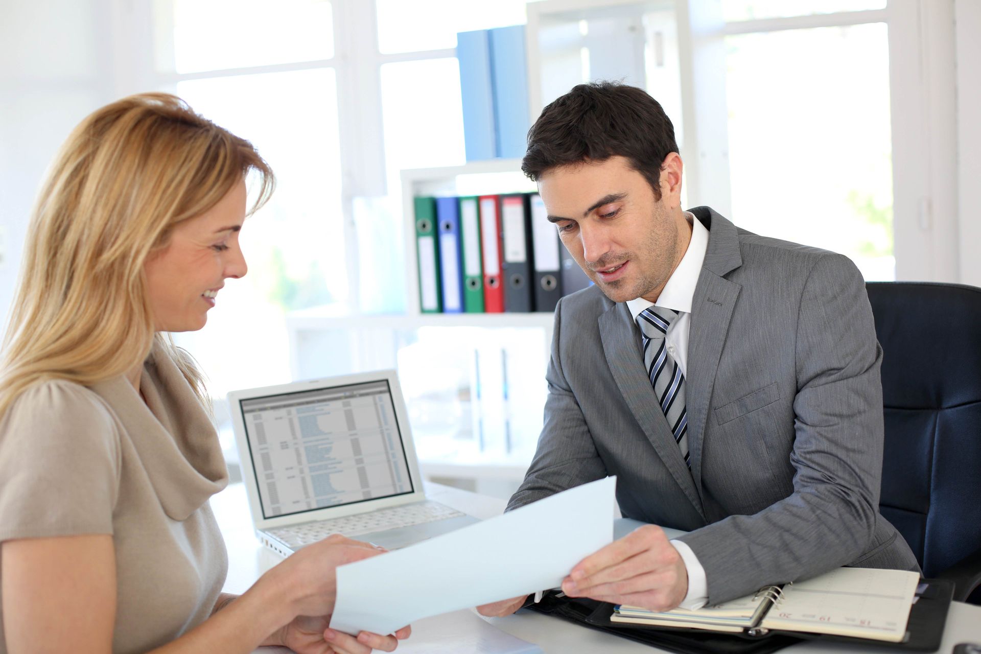 a man and a woman are sitting at a desk looking at a piece of paper