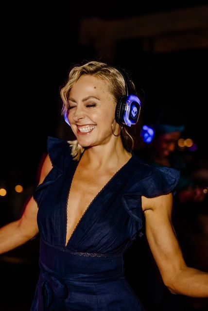 A woman in a blue dress is wearing headphones and smiling.