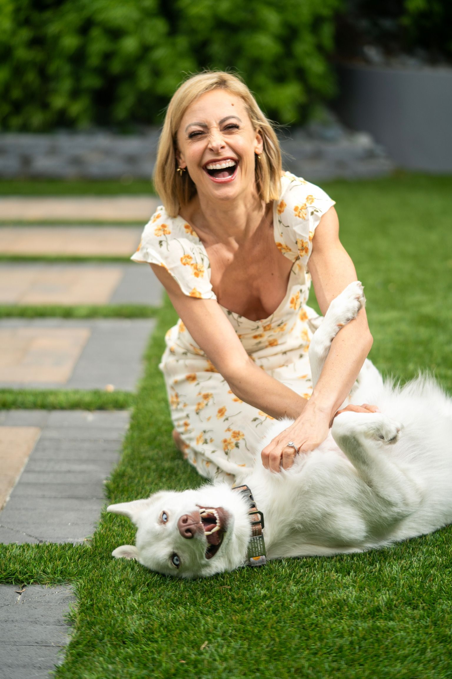 A woman is playing with a white dog on the grass.
