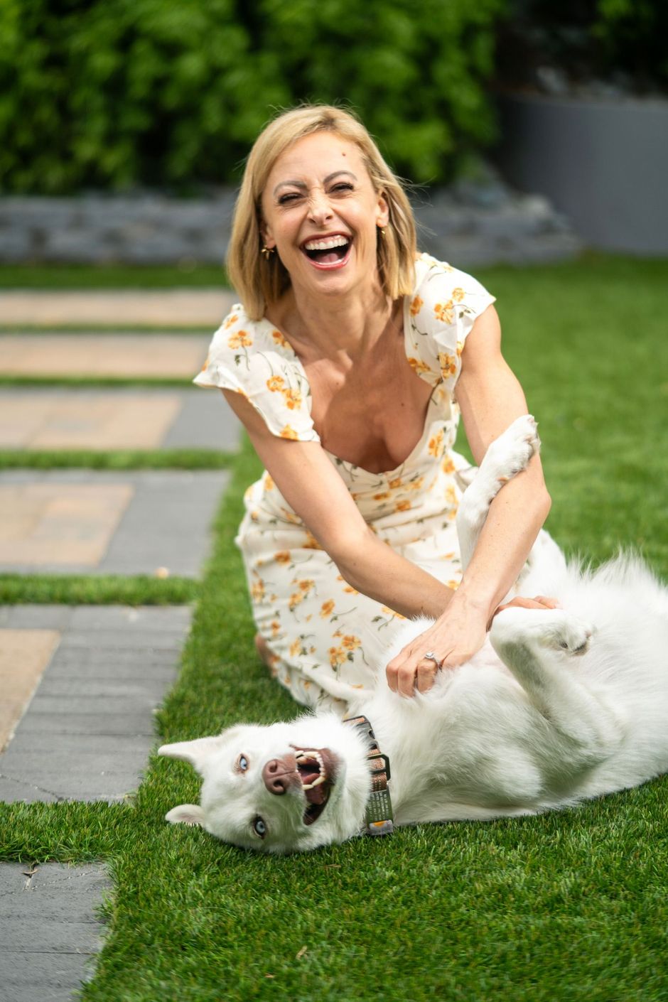 A woman is playing with a white dog on the grass.