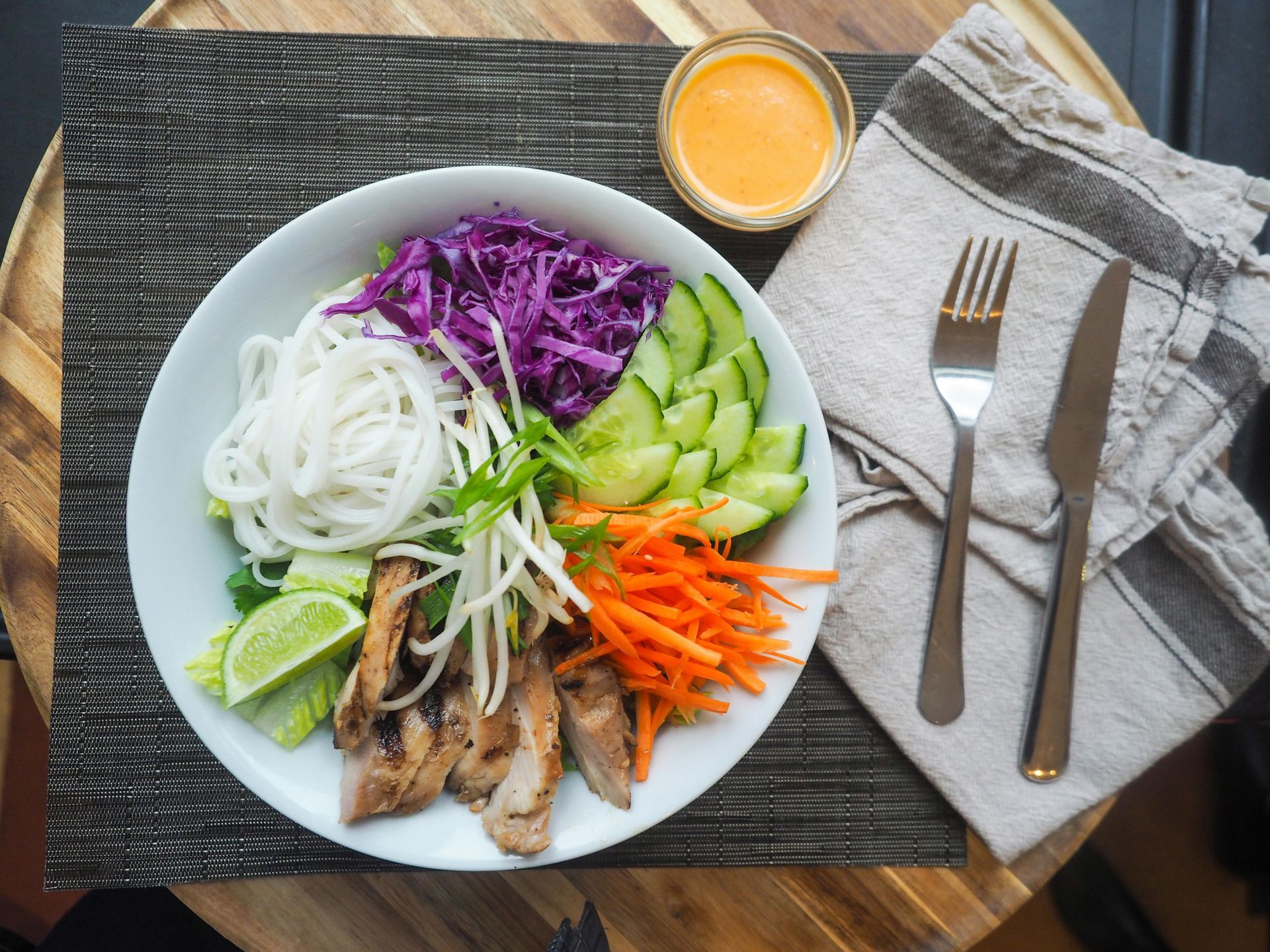 A plate of food with noodles , meat , vegetables and sauce on a table.