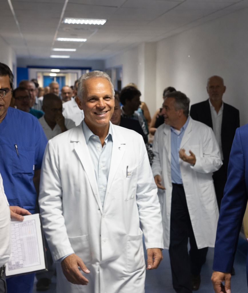 Medico in camice bianco seduto alla scrivania, che guarda un computer portatile. Ambiente di studio medico con documenti e stampante.