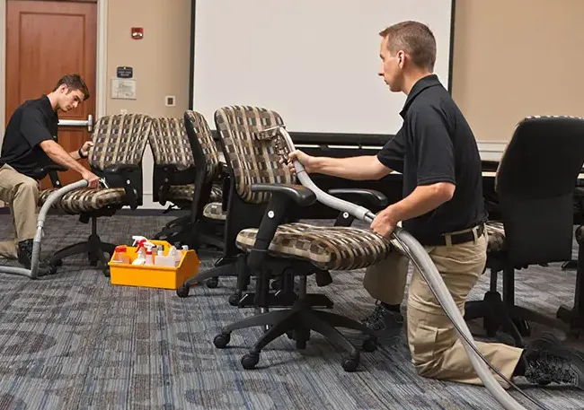 Two men are cleaning chairs in a conference room