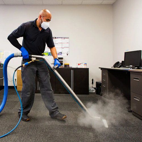 A man wearing a mask is using a vacuum cleaner to clean a carpet