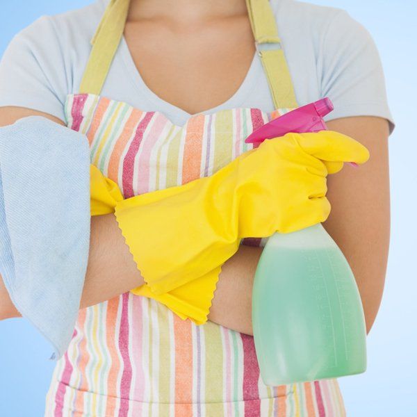 A woman wearing a striped apron and yellow gloves holds a spray bottle