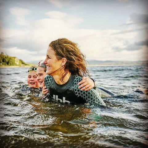 Jo in the sea at Tralee with her 2 children behind her. Oldest daughter is holding on to mum's shoulders. Younger daughter in next to her big sister.