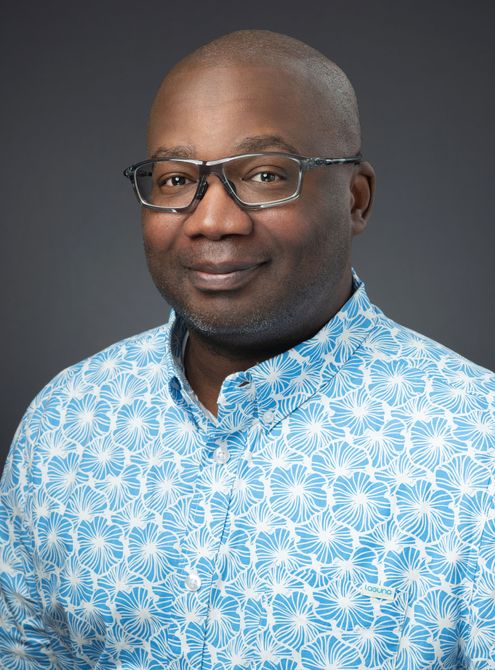 A man wearing glasses and a blue shirt is smiling for the camera.