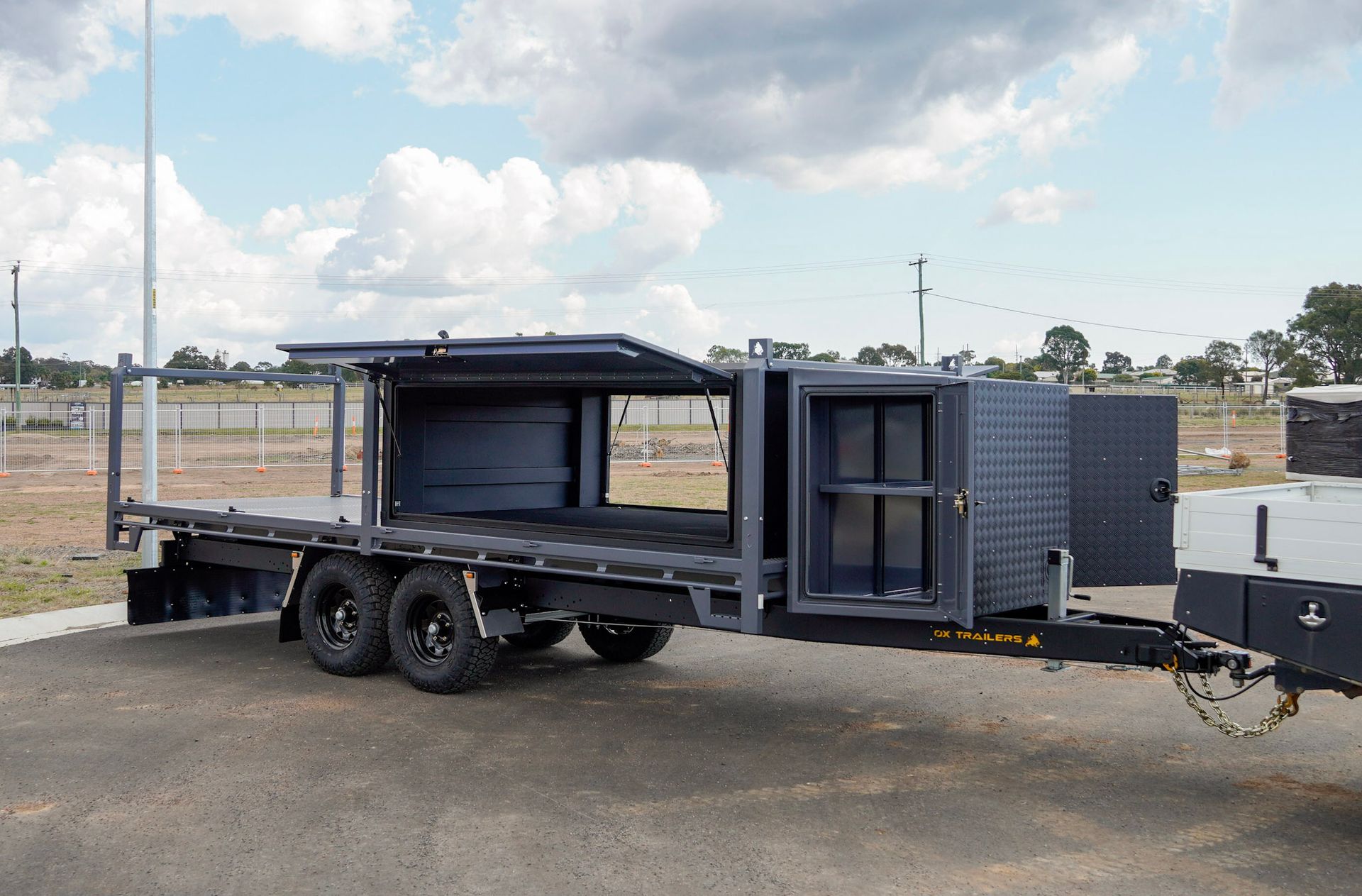 heavy duty custom flat top trailer for gee building at rural construction site with toolbox and canopy doors open.