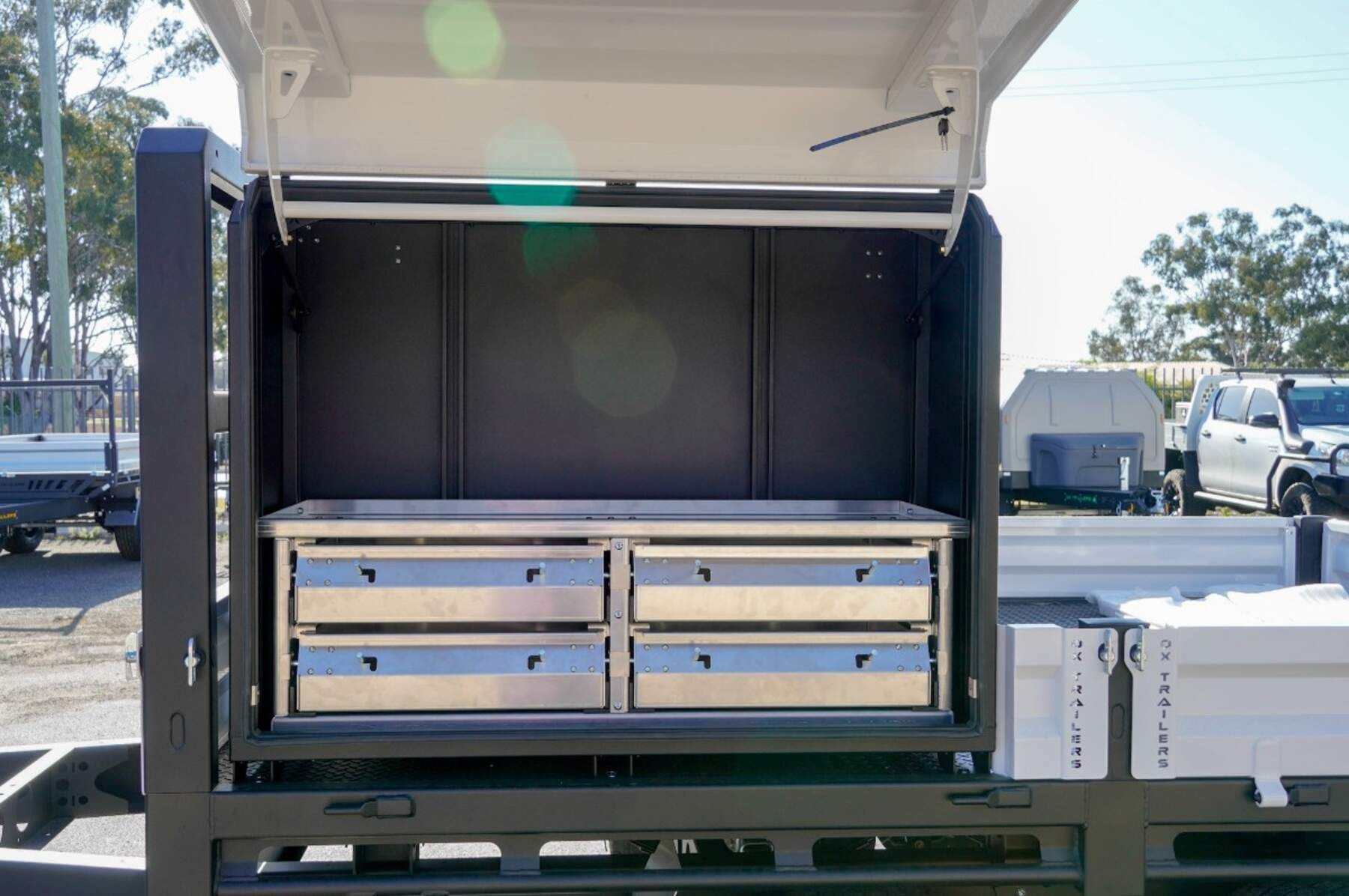 heavy duty custom flat top trailer for gee building at rural construction site with toolbox and canopy doors open.