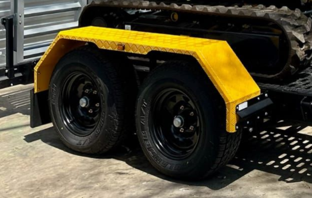 The bright yellow mudguard of an ox plant trailer, coloured to match machine that it is hauling.