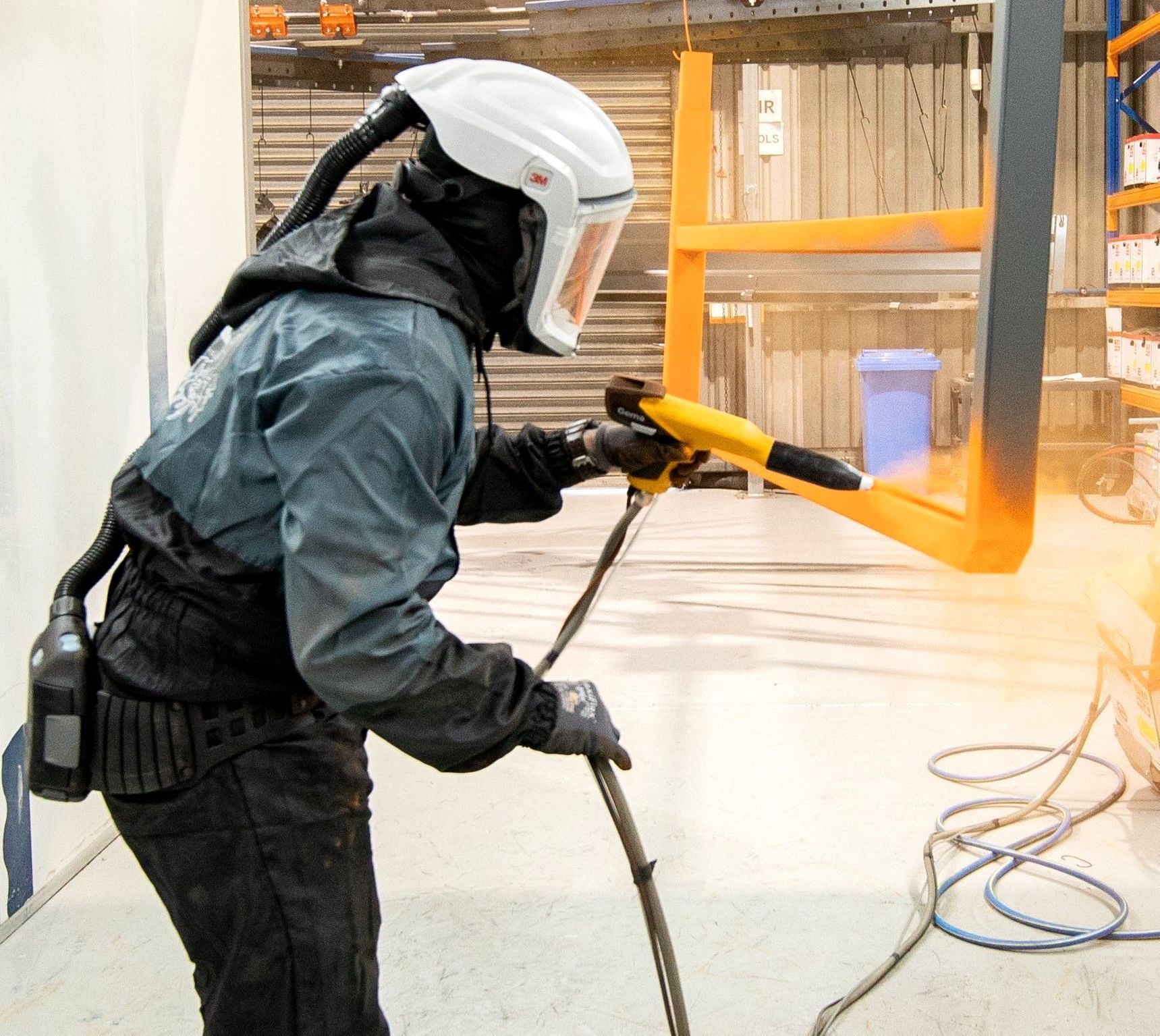 Experienced coater spraying final coat of Orange on trailer accessory.
