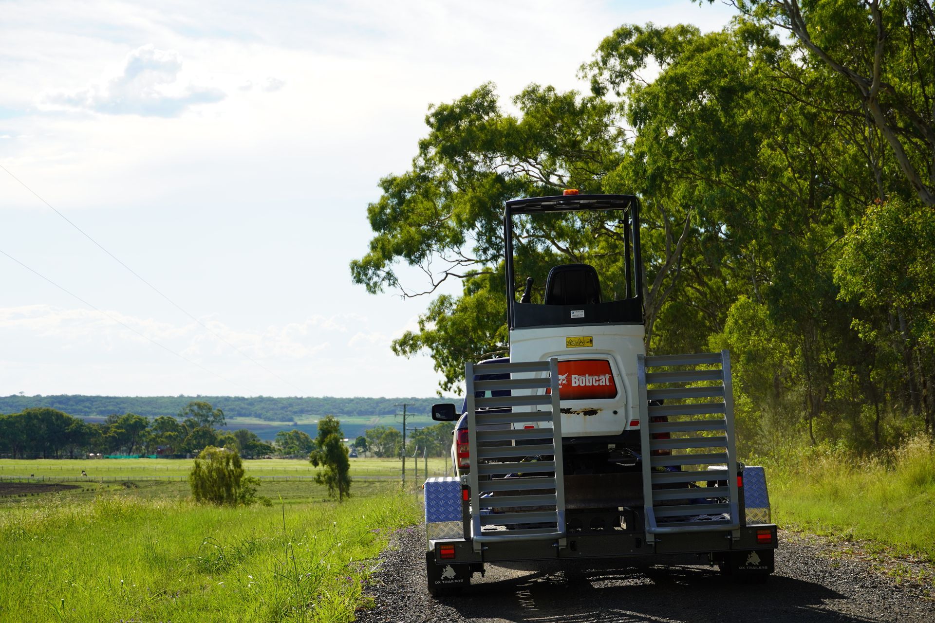 A plant trailer carrying an excavator driving away from the camera, the ox trailers mudguards are in full view.