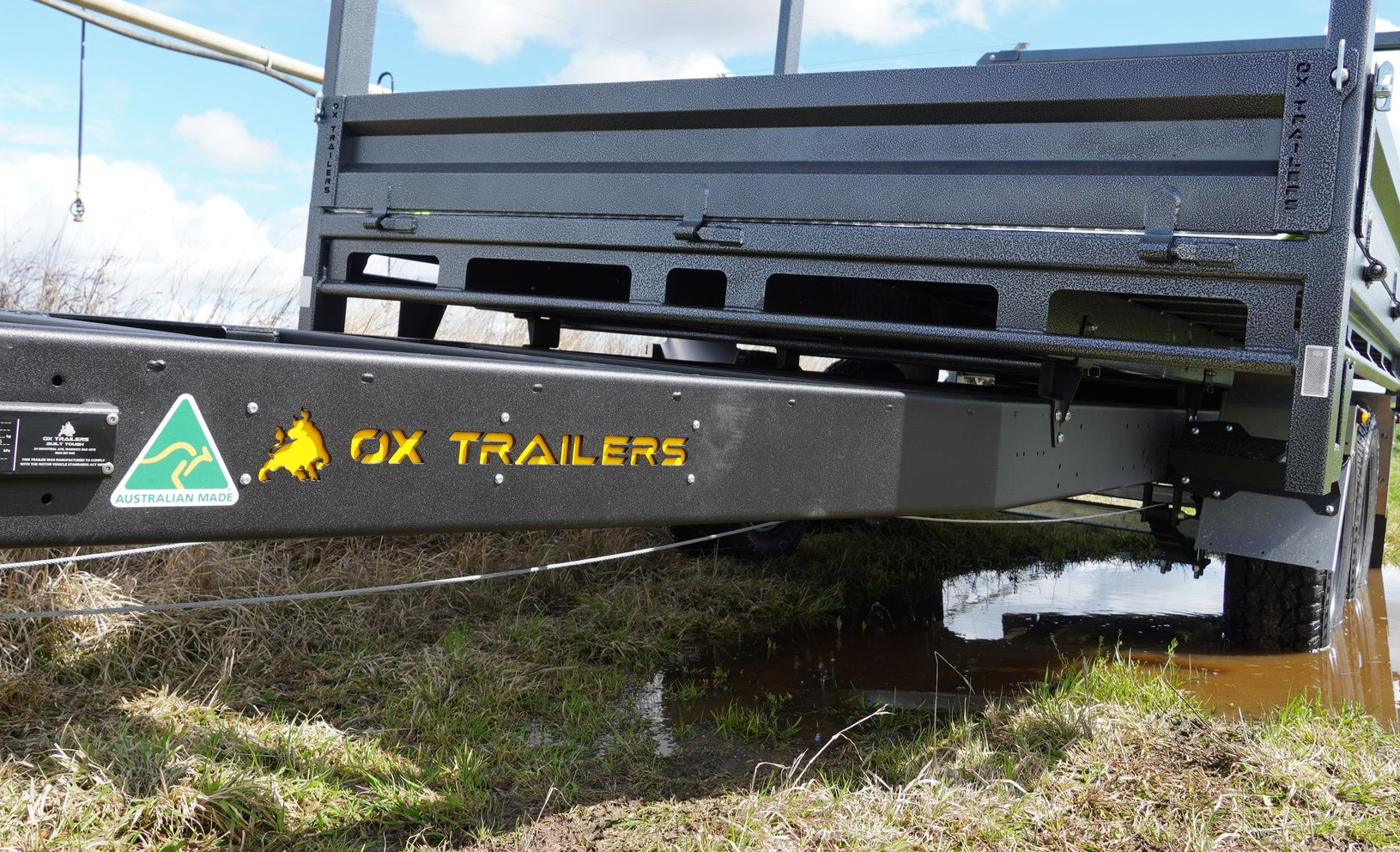 Heavy-duty Australian-made ox trailer in the mud of a rural farm, with a green and gold Australian-made sticker on the chassis.