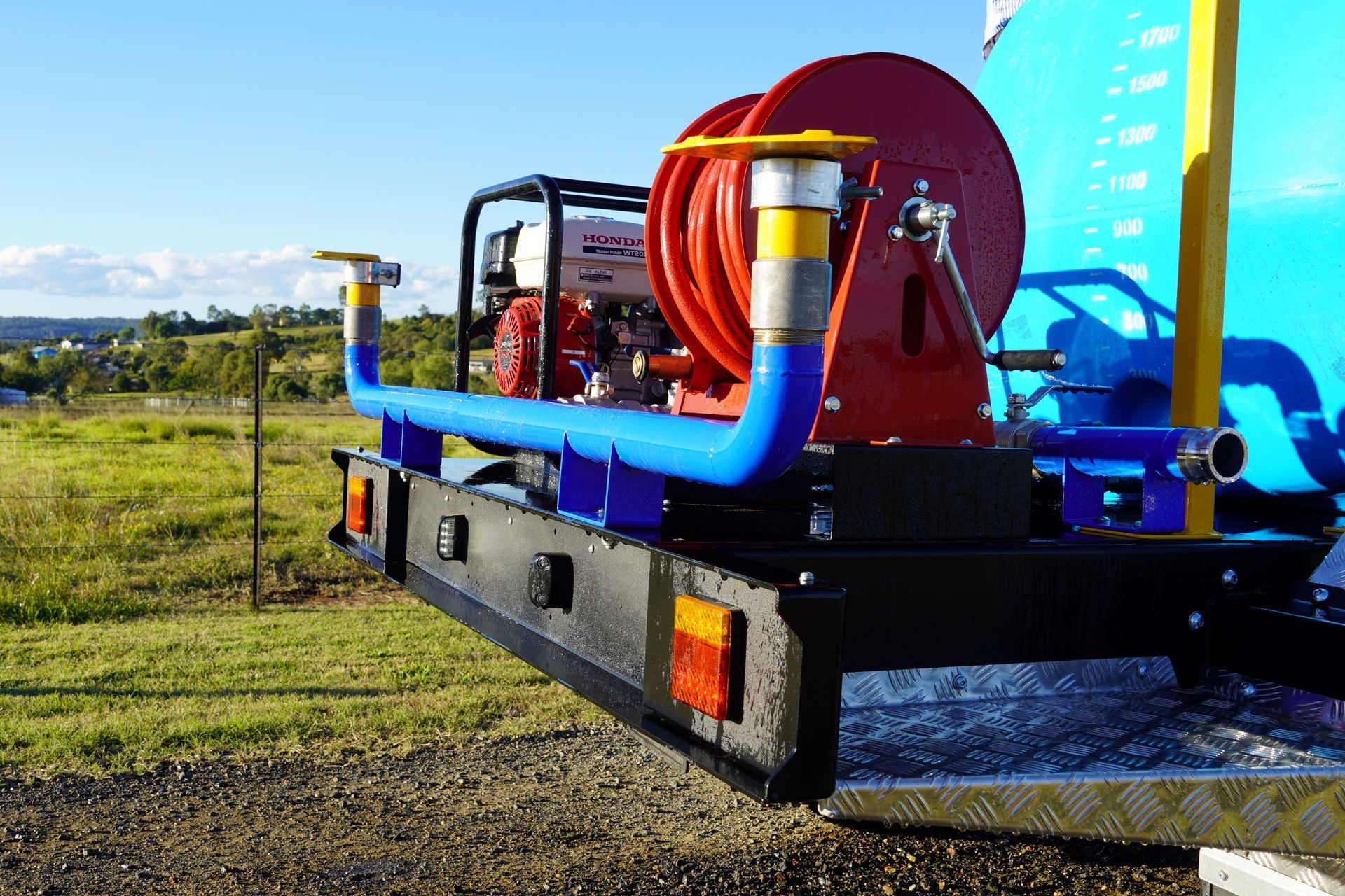 A side view of the water trailer as the deflector side sprayers are activated and in use on a dirt road.