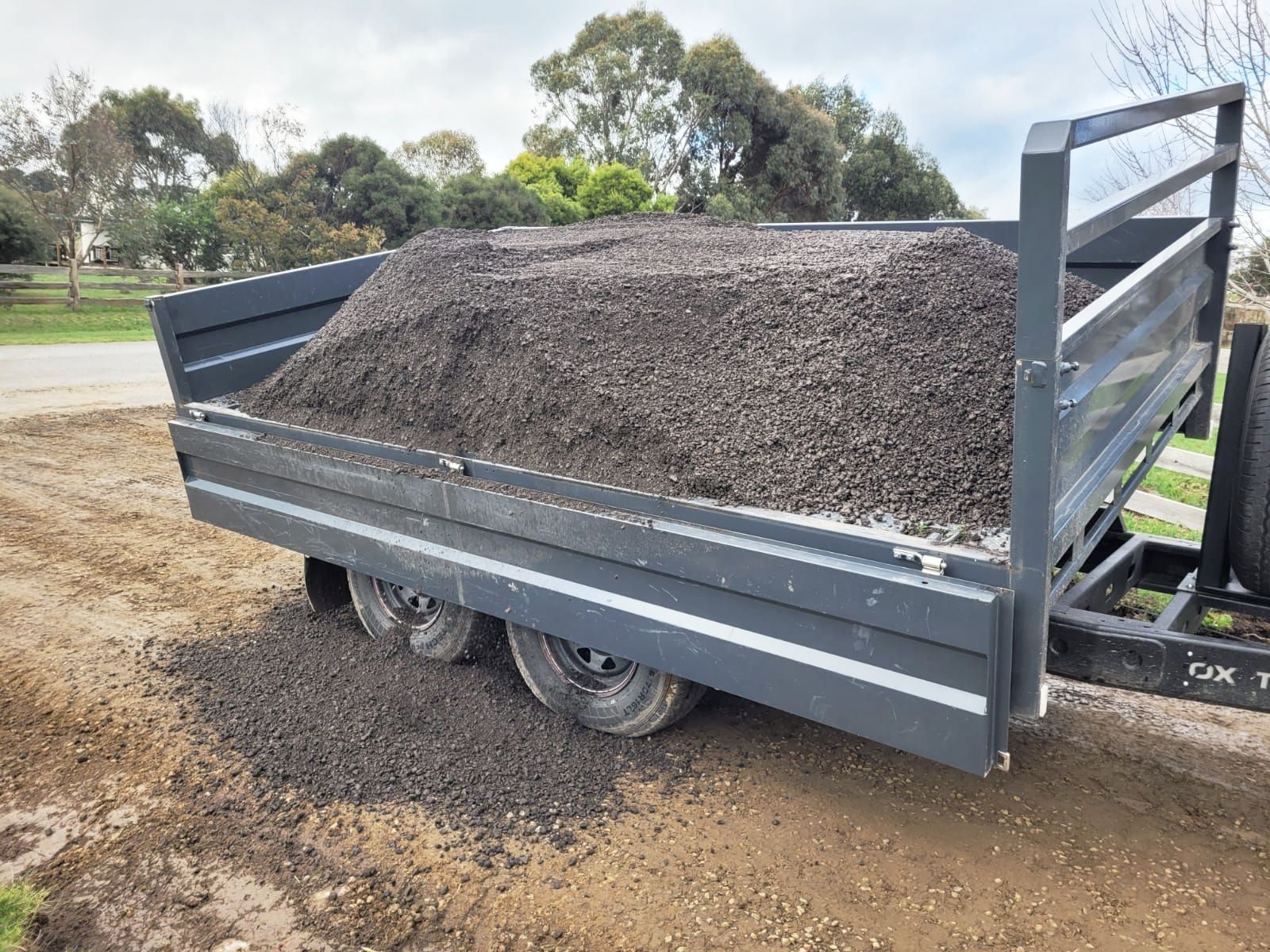 A side tipping trailer beginning to tip gravel out from the right hand side, with the long dropside unlatched.