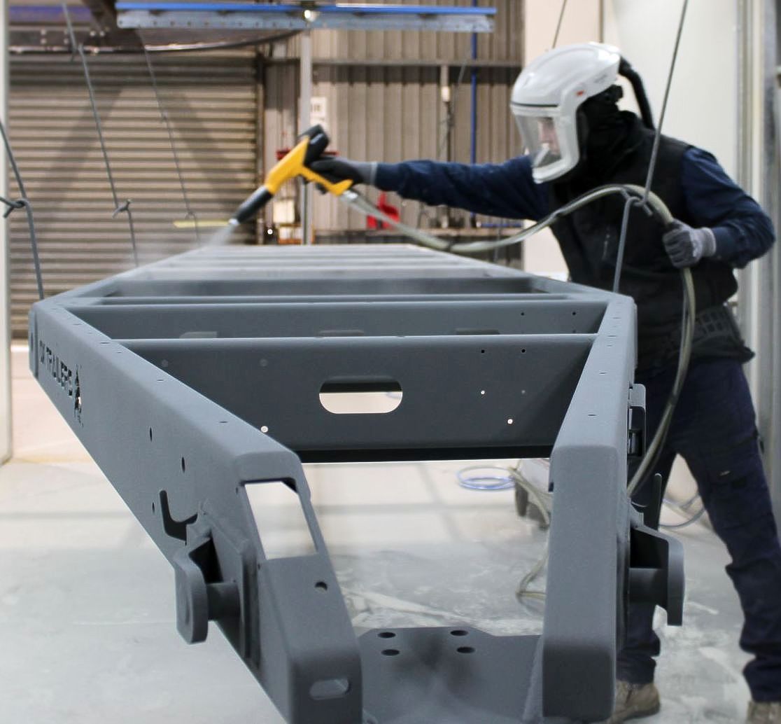 Professional coater spraying trailer chassis with primer, sealing it from any elements.